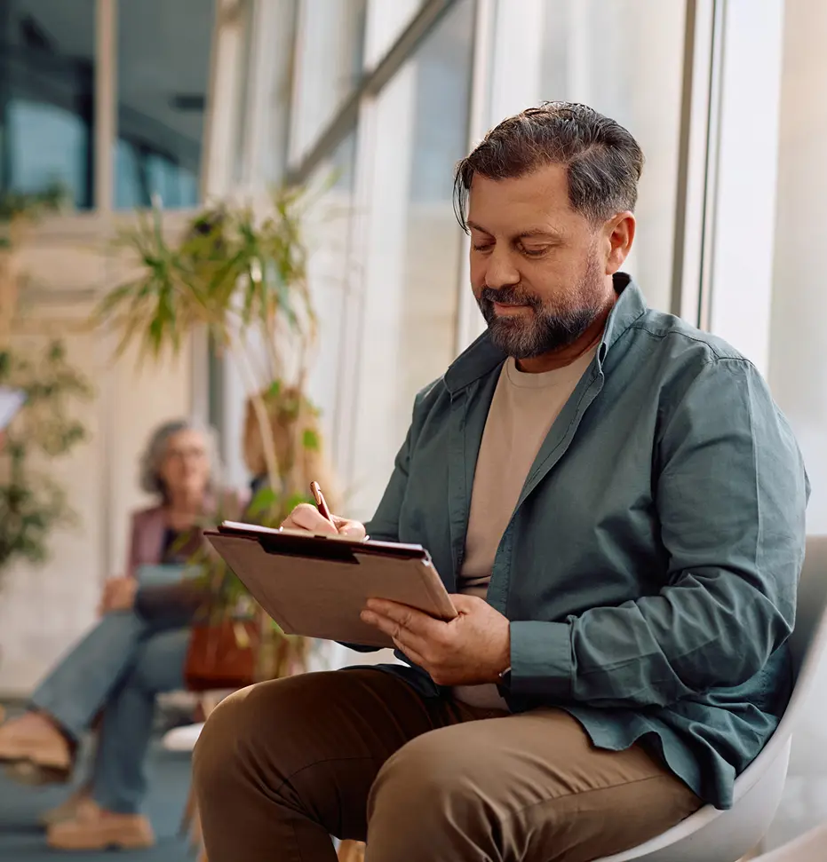 Man seated with clipboard, indoor plants nearby