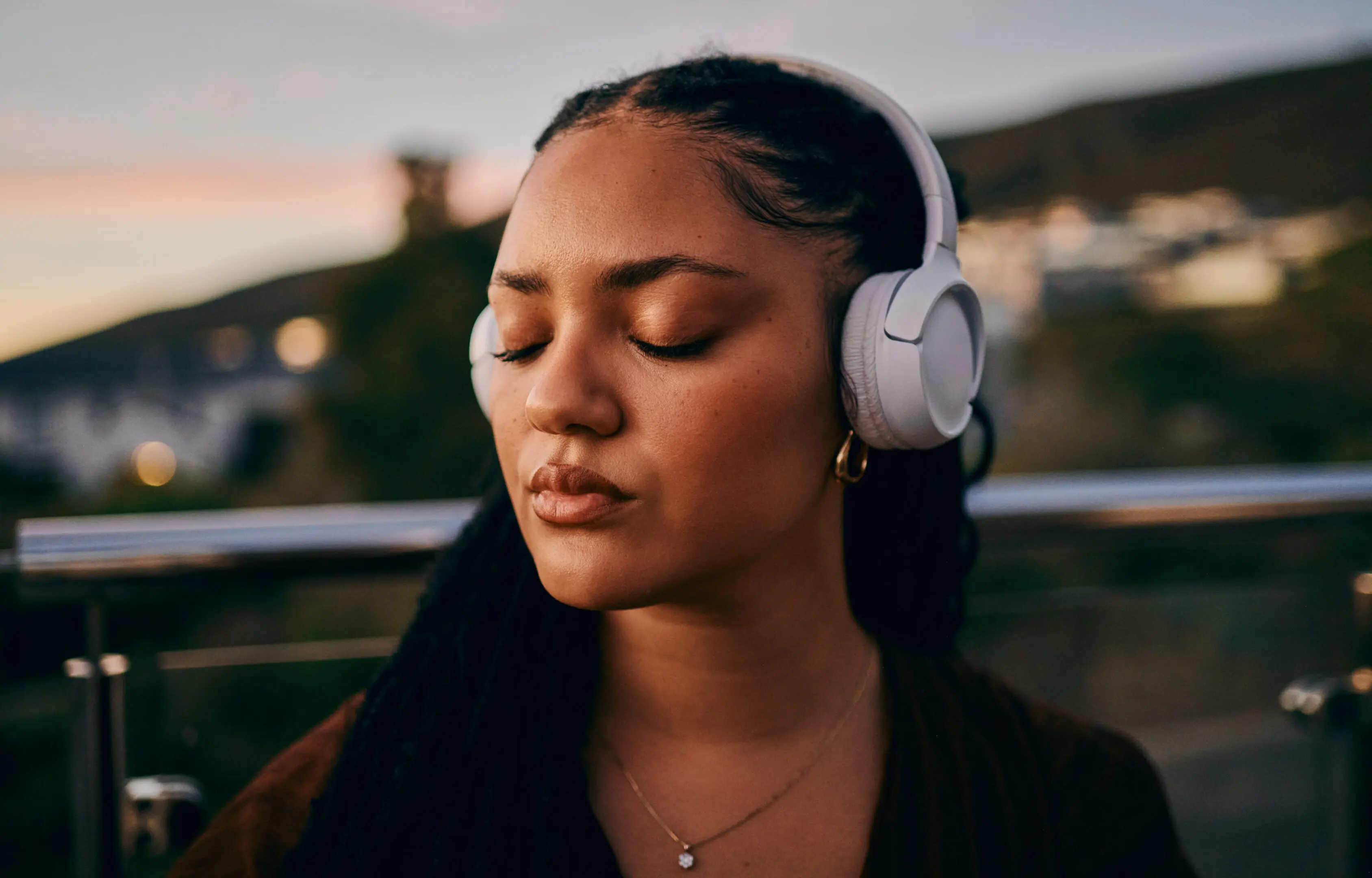 Woman with closed eyes listening to music on headphones outdoors.