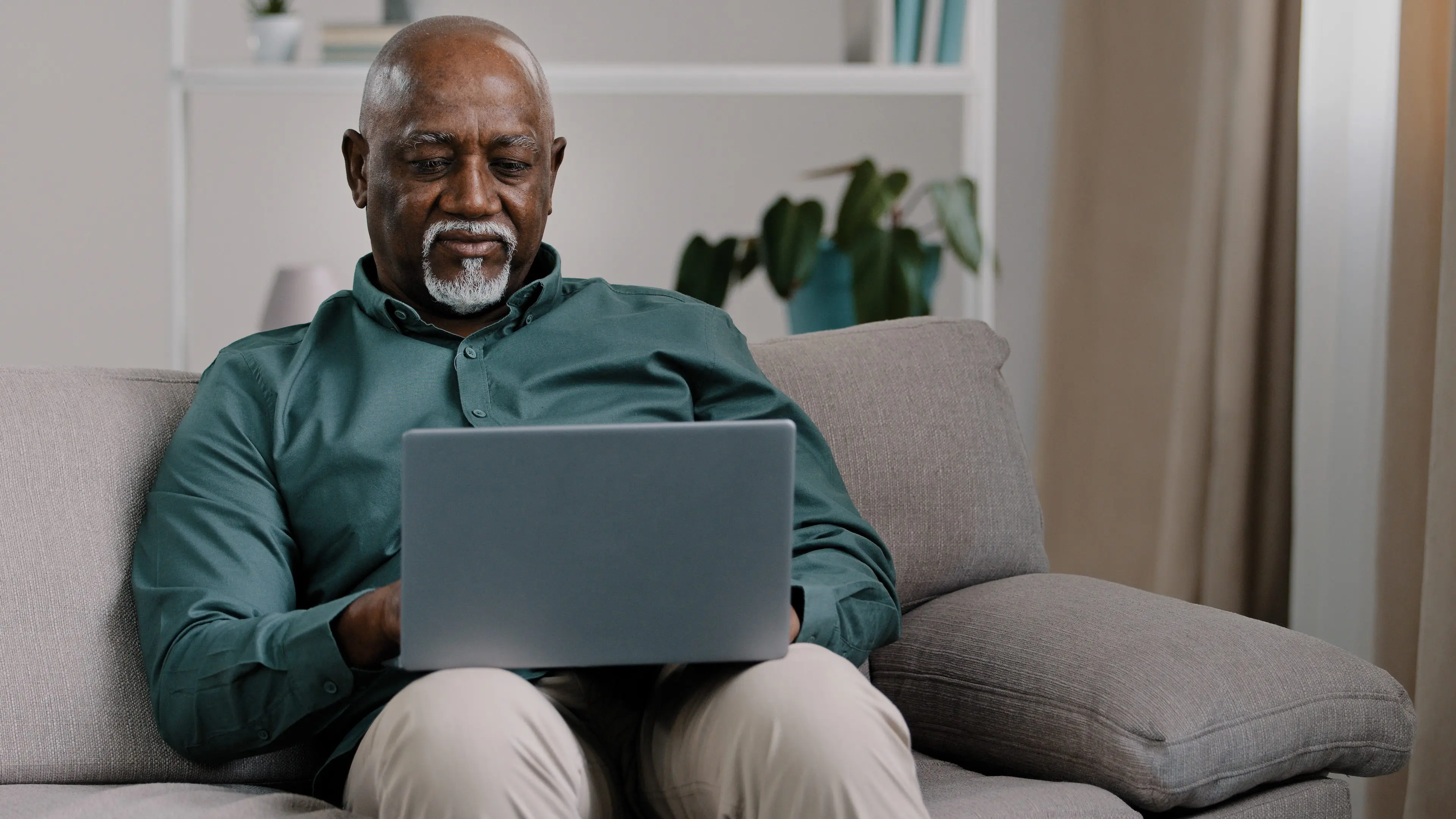 African American bald bearded businessman teacher writer entrepreneur checking data online use computer application connection wifi network at home office sitting on comfortable sofa typing on laptop. High quality photo