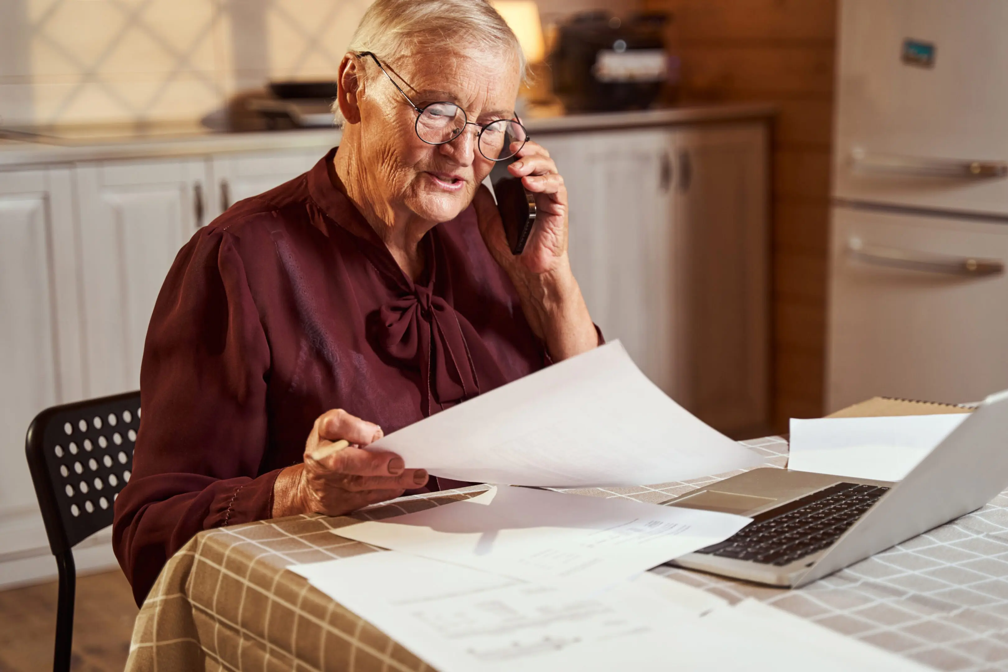 Aging person in glasses looking at her paperwork and checking data through mobile phone with colleagues