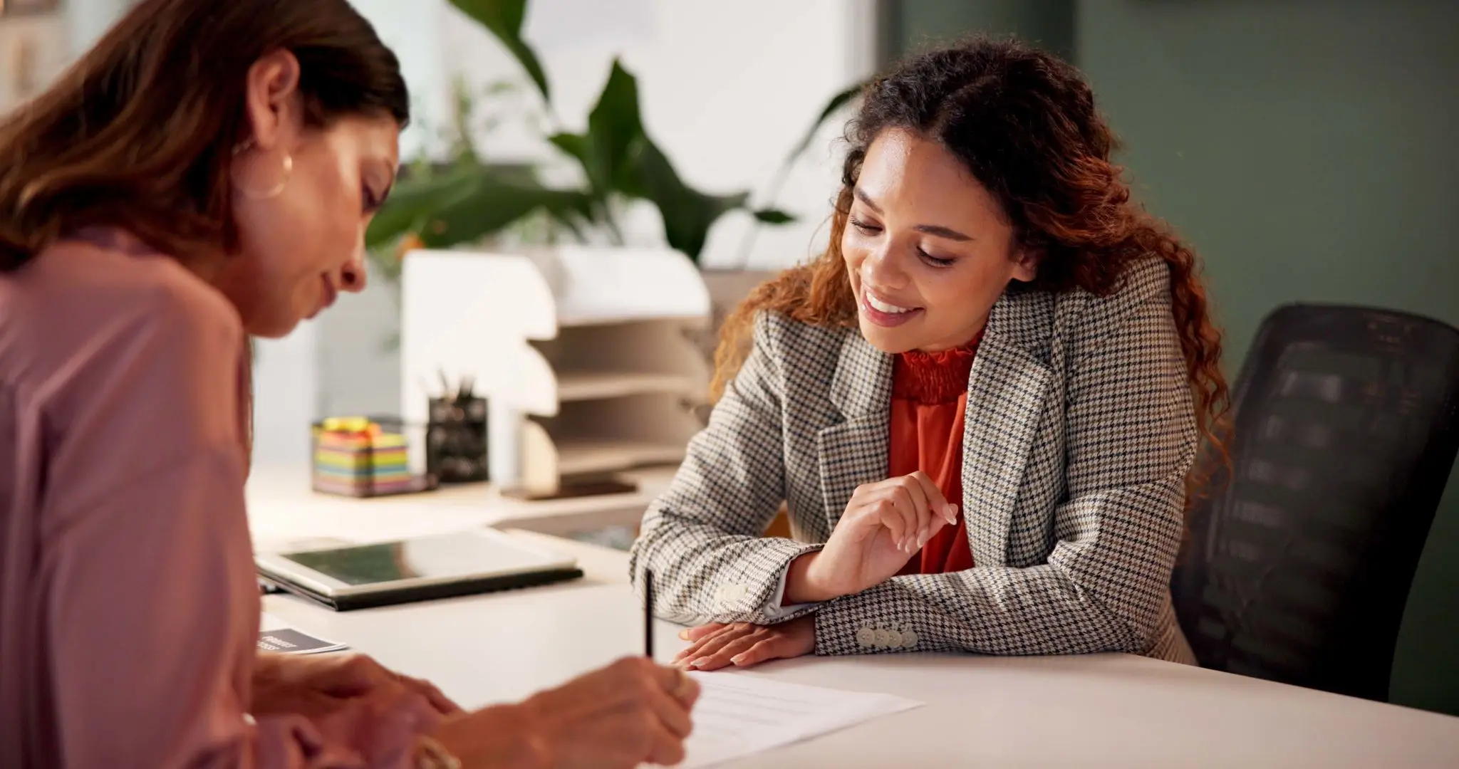 A woman smiling and discussing with a colleague in an office.
