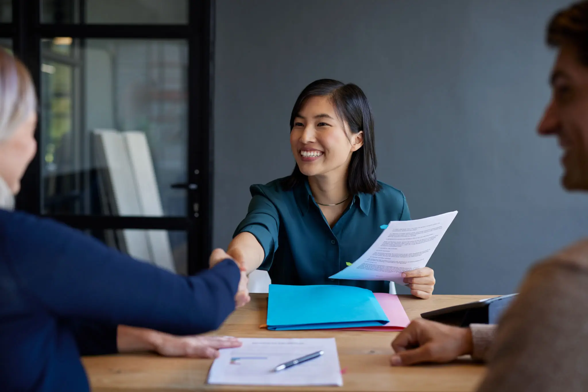 Woman smiling and shaking hands in a professional setting.