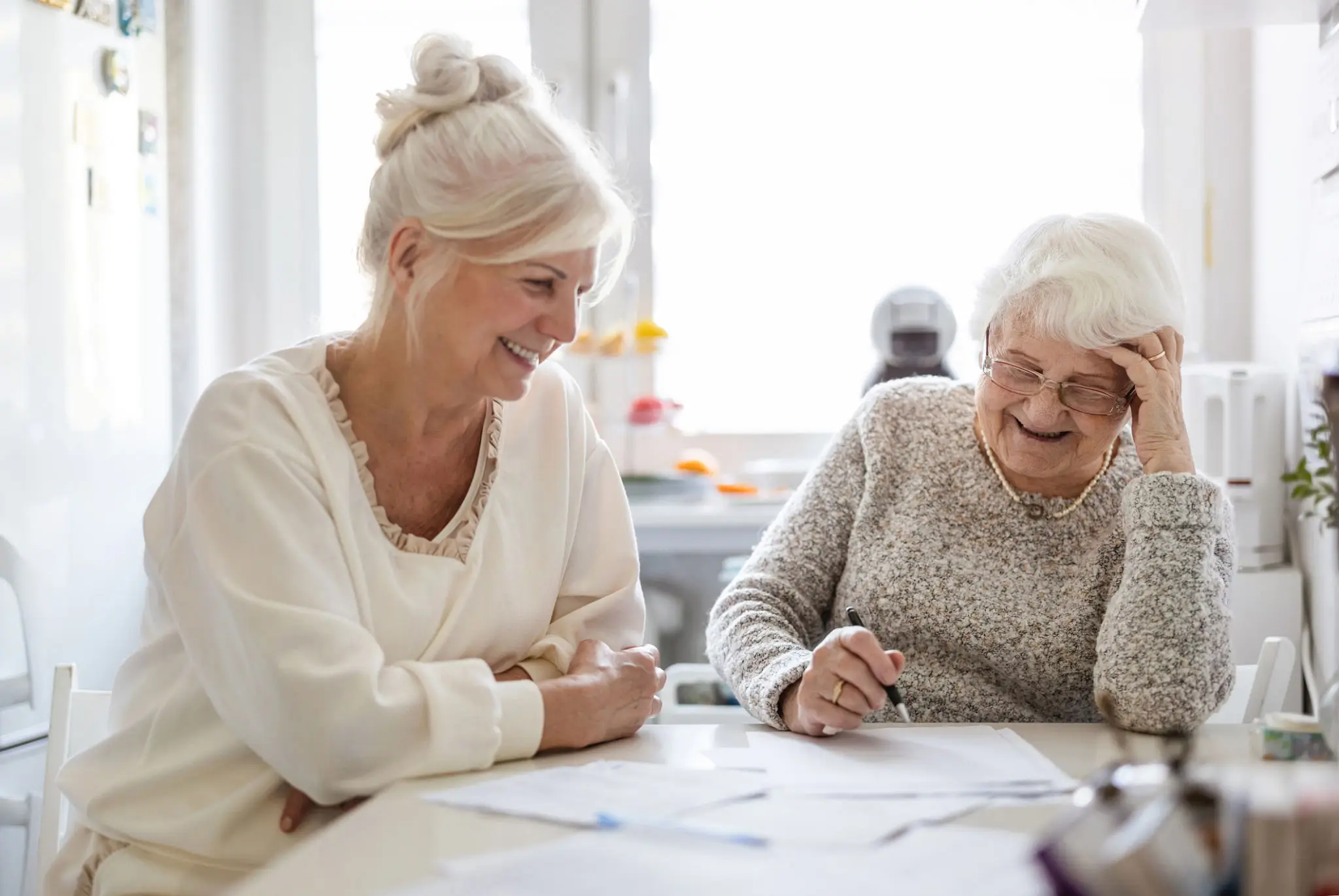 Older woman and younger woman happily working on paperwork together.