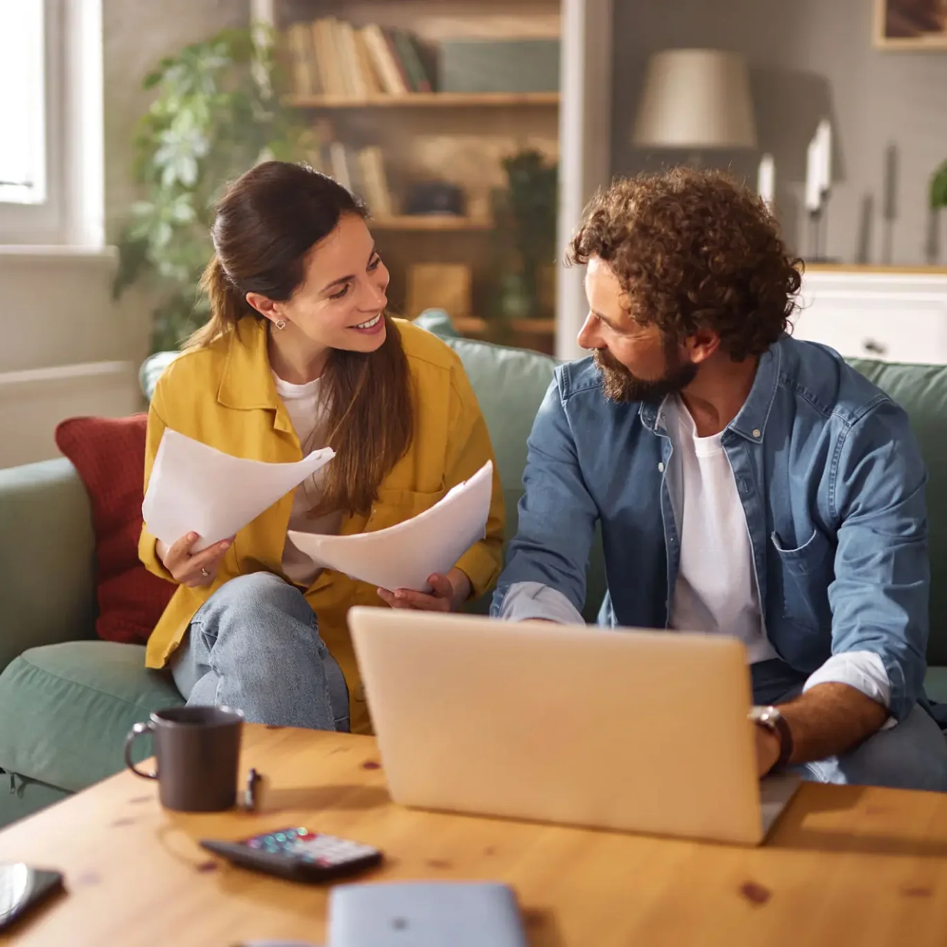 Two people discussing work with laptop and documents in a cozy room.