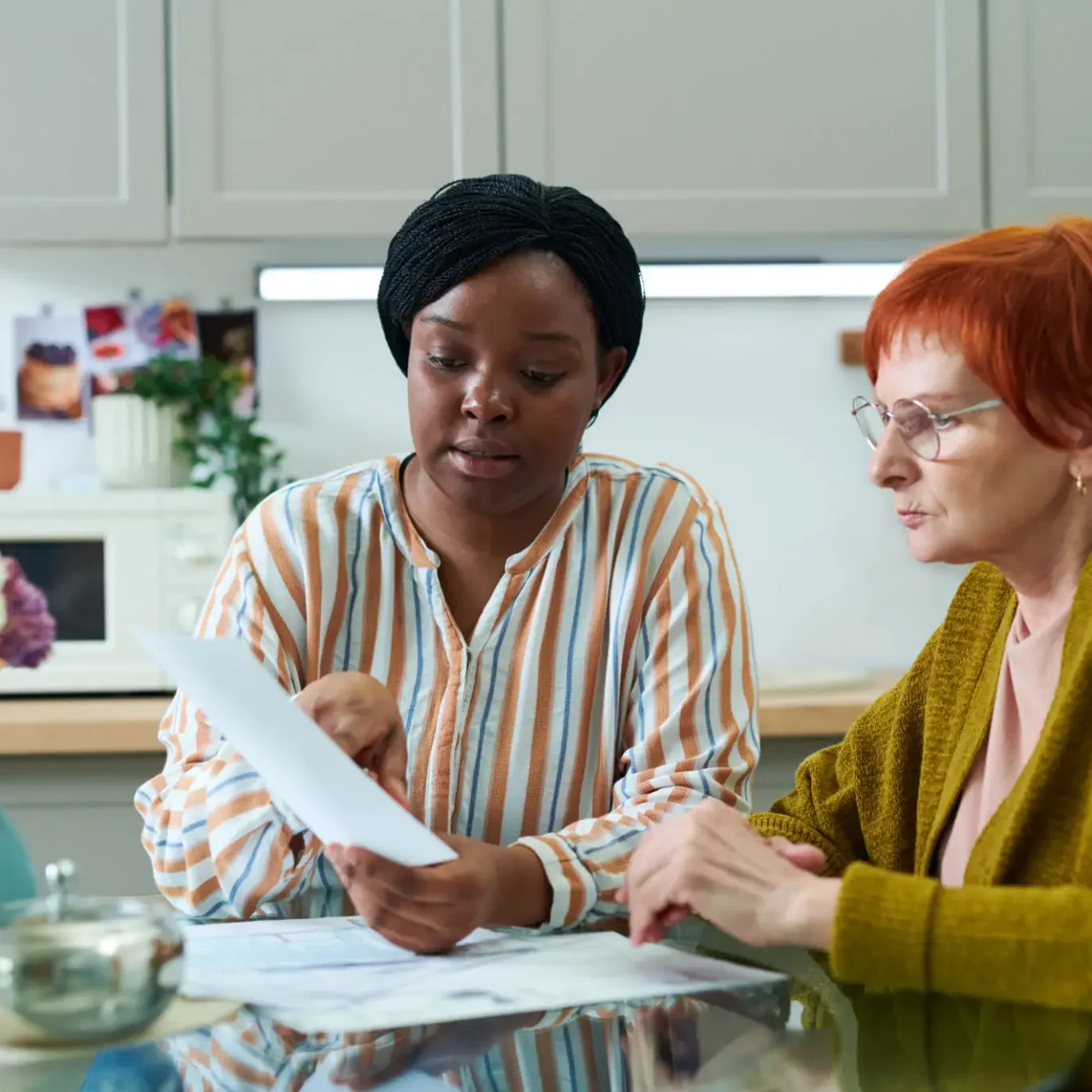Two women discussing a document in a kitchen setting.